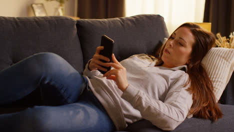 Close-Up-Of-Woman-Lying-On-Sofa-At-Home-At-Streaming-Or-Watching-Movie-Or-Show-Or-Scrolling-Internet-On-Mobile-Phone-1